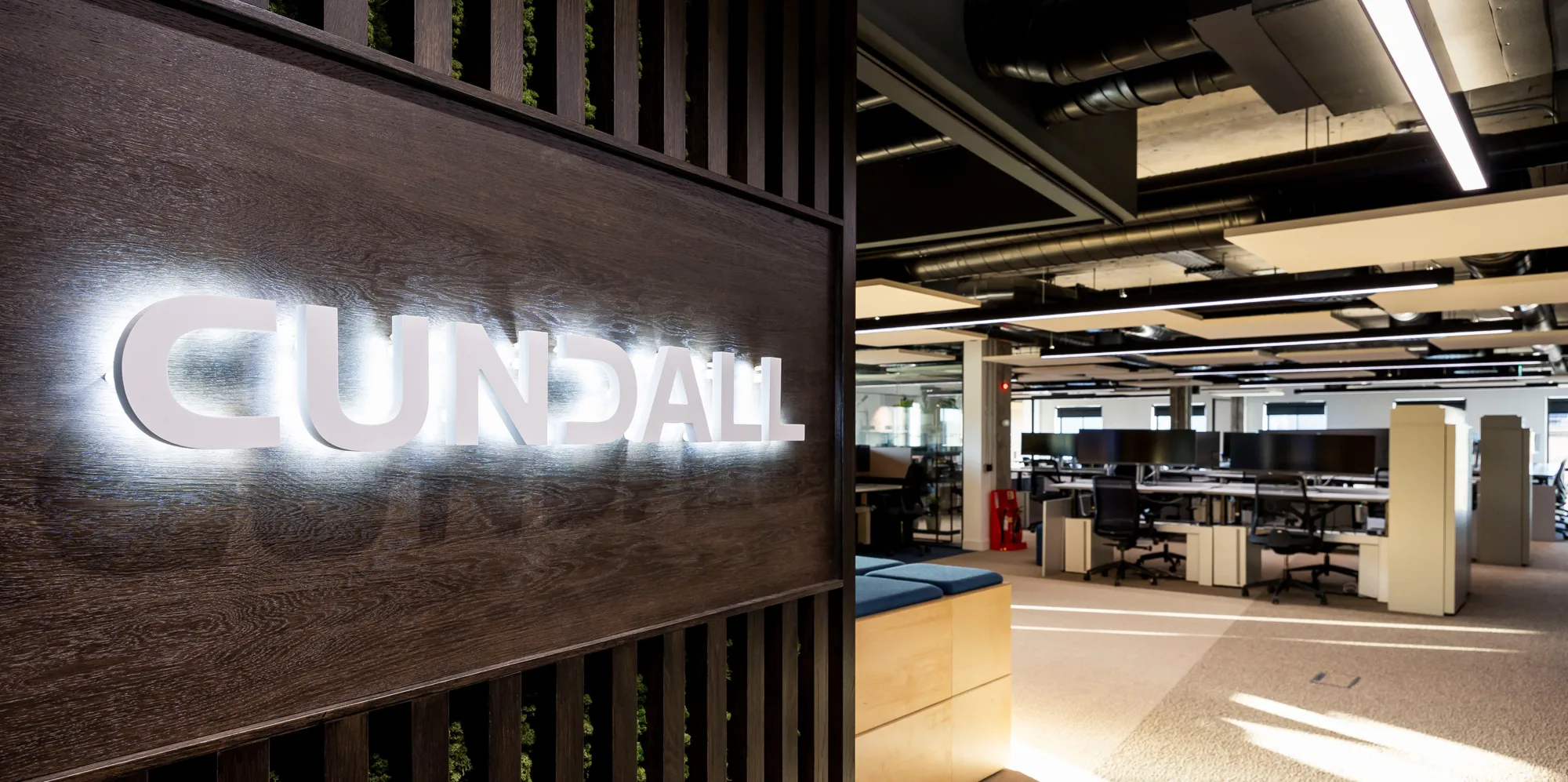 Interior entrance of the office with a illuminated Cundall logo on a dark wooden panel.