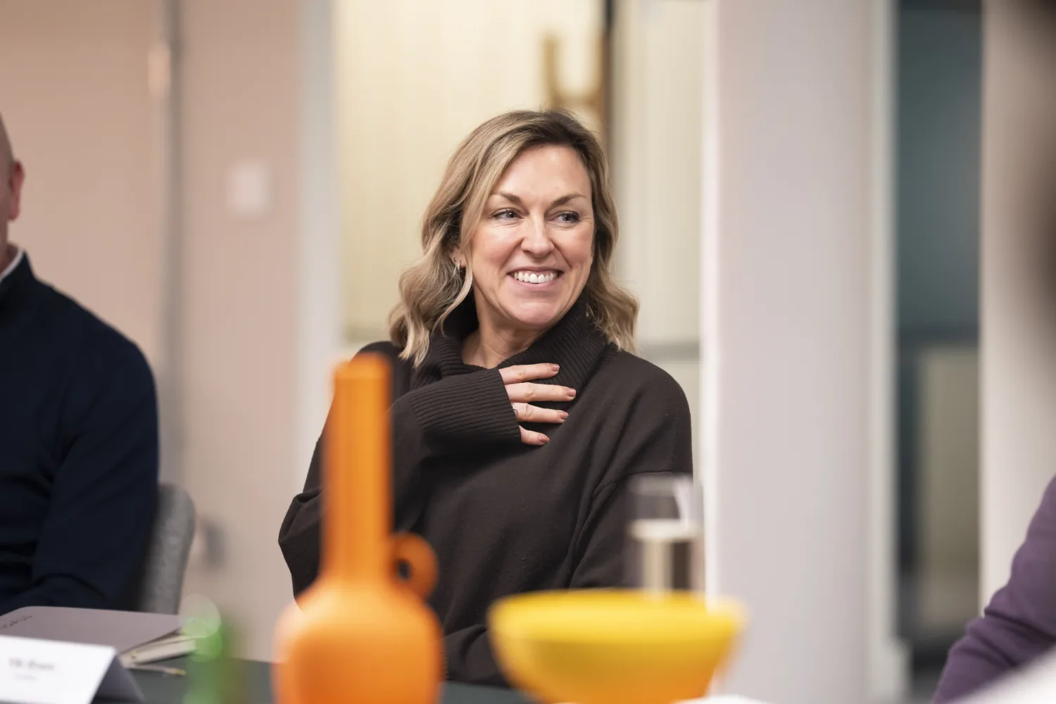 Person sat at table laughing with orange vase in foreground