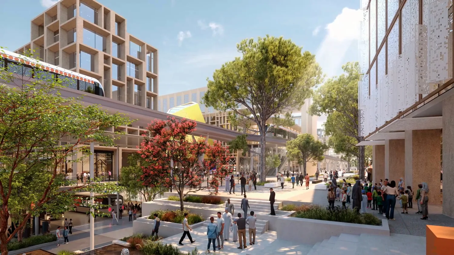 Urban plaza with modern buildings featuring grid-like facades, glass windows, and shaded walkways. Numerous people walk and gather on steps and paths, surrounded by trees, flowering plants, and a raised transit line overhead.