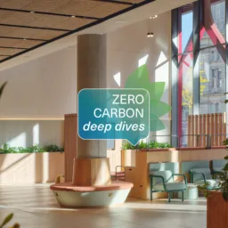 Bright, modern interior atrium with timber seating, planters, and green chairs around a central column. Large windows reveal an urban street outside. Overlaid graphic reads ‘ZERO CARBON deep dives’.