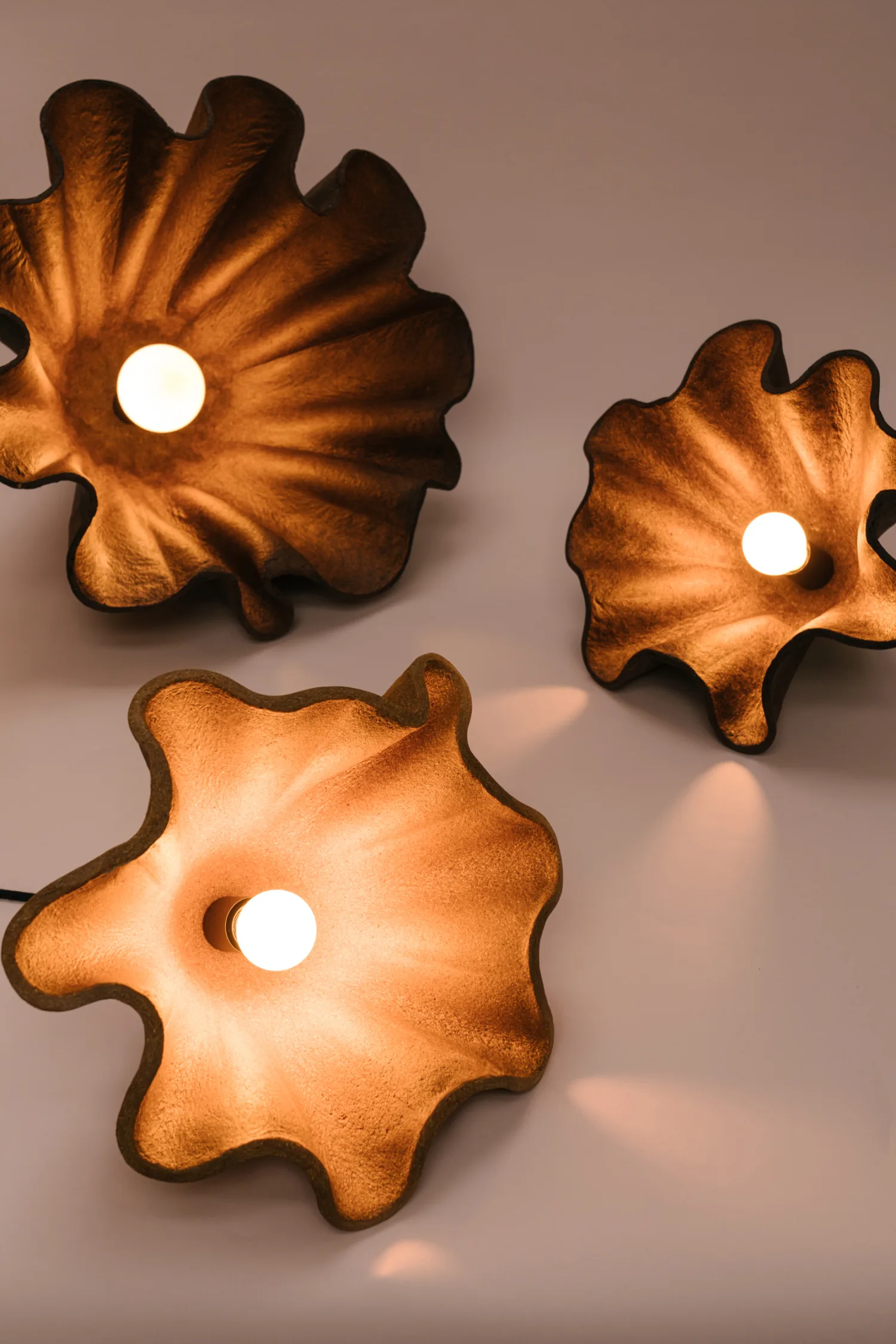 Three Obscure lampshades resting on a beige surface facing upwards