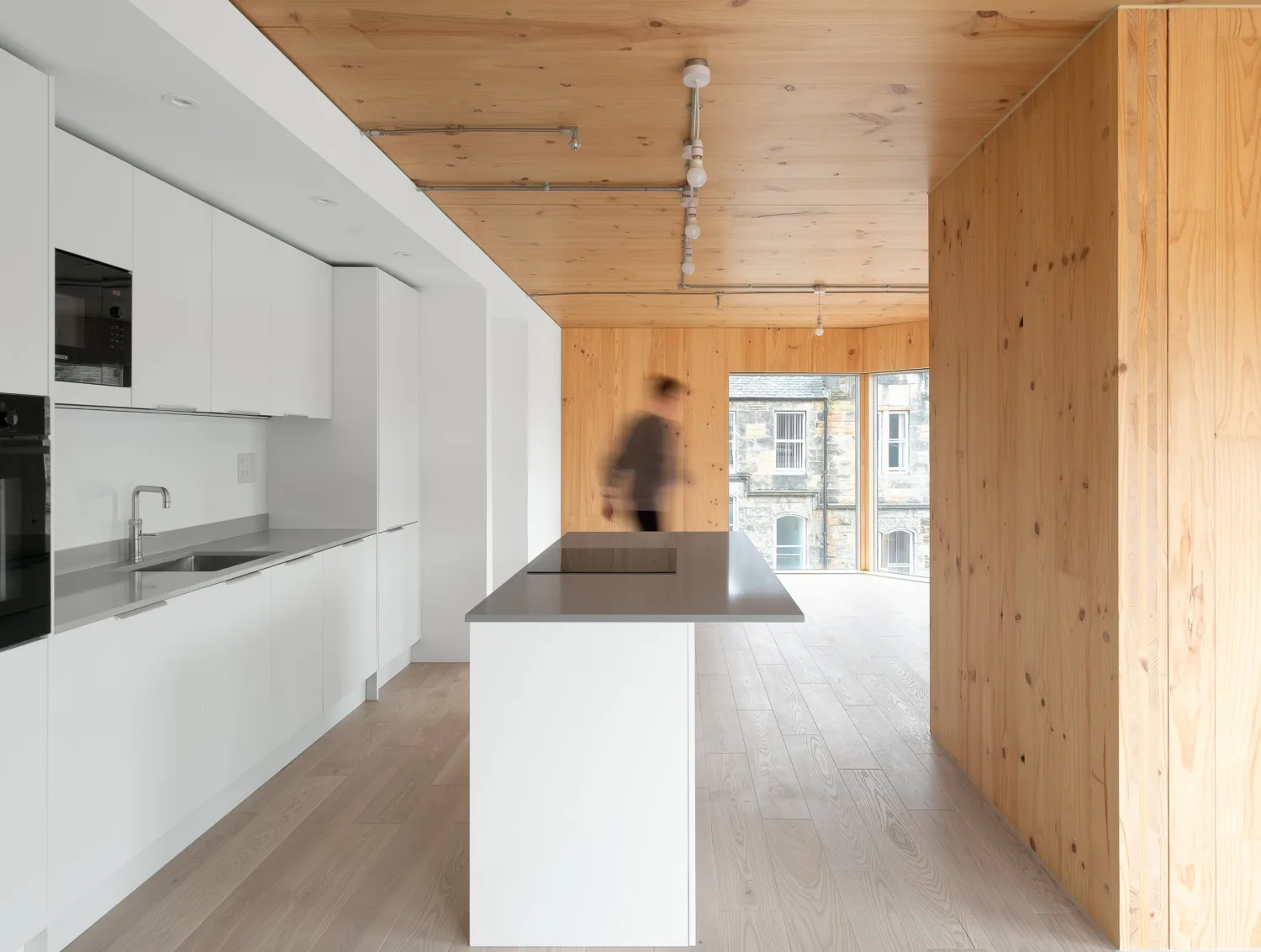 Interior of a kitchen with white units, and wooden ceiling, floors and walls