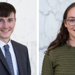 Two side‑by‑side portrait photos against a light marble background: on the left, a person in a dark suit, white shirt, and patterned tie; on the right, a person in a textured green buttoned top with layered necklaces.