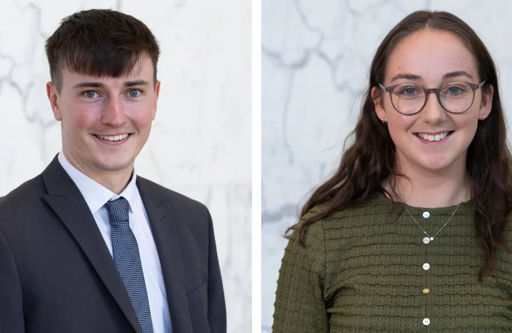 Two side‑by‑side portrait photos against a light marble background: on the left, a person in a dark suit, white shirt, and patterned tie; on the right, a person in a textured green buttoned top with layered necklaces.