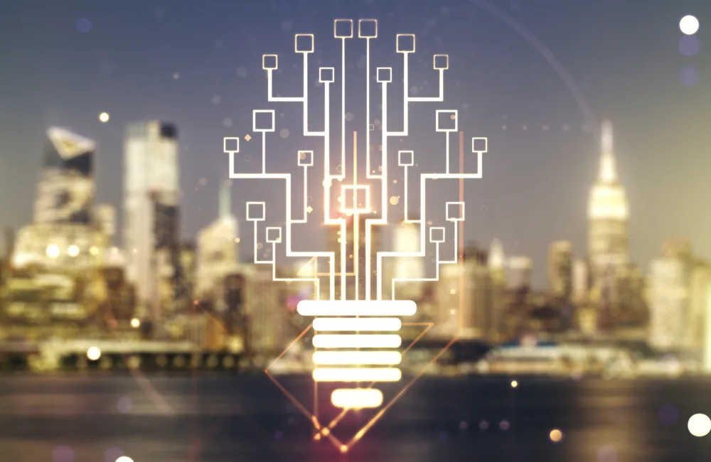 A glowing graphic of a lightbulb formed by interconnected circuit-like lines and nodes overlays a blurred city skyline at night, with illuminated buildings and reflections on water in the background.