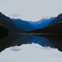 Silhouettes in blue and black of mountains reflected in a still lake