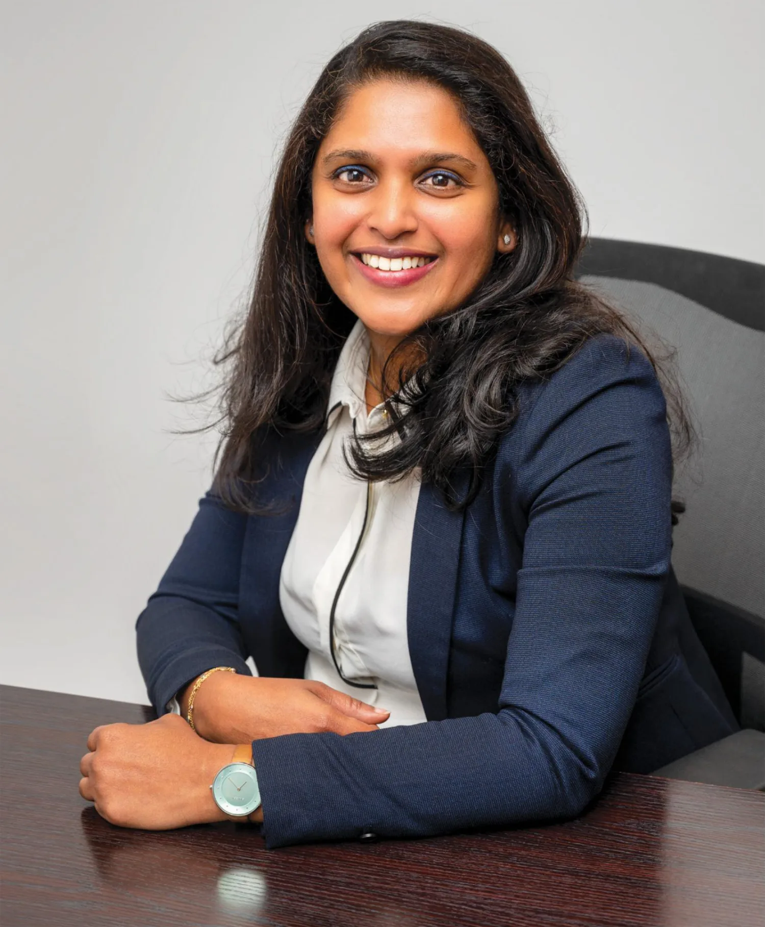 Smitha Mathew smiling in front of the camera while leaning on a wooden desk