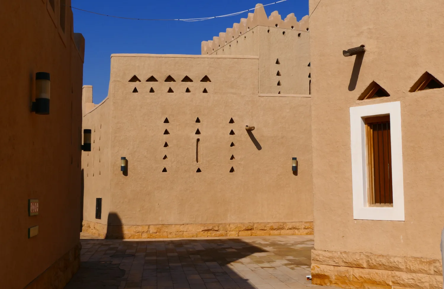 a {     text-decoration: none;     color: #464feb; } tr th, tr td {     border: 1px solid #e6e6e6; } tr th {     background-color: #f5f5f5; }   Sunlit alley between sand-colored buildings with geometric cut‑out patterns, wooden window frames, wall-mounted lights, and a paved stone walkway under a clear blue sky.