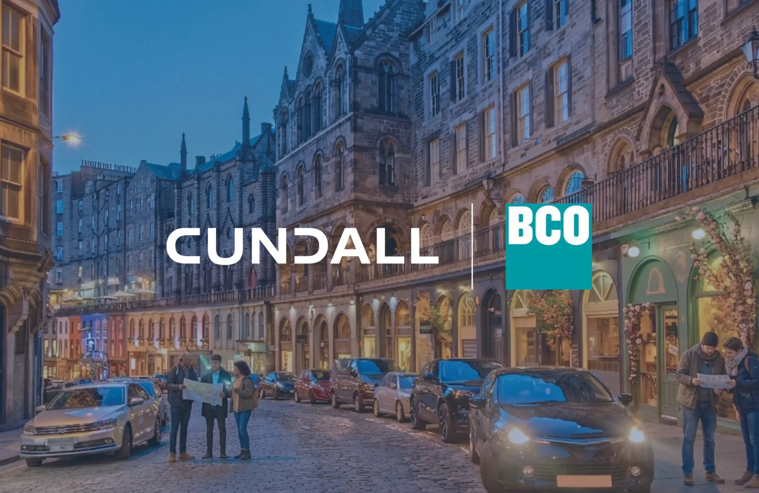 Street scene with historic stone buildings, parked cars, and several people standing on a cobblestone road. The image includes the visible text ‘CUNDALL’ and a blue box with the text ‘BCO.