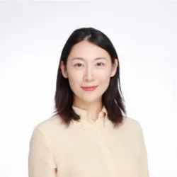 Studio-style head-and-shoulders portrait of a person wearing a light beige buttoned blouse, with straight shoulder-length dark hair, centred against a plain white background.