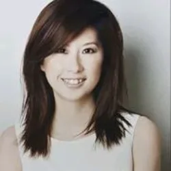 Head-and-shoulders studio portrait of a person with straight, shoulder-length dark hair wearing a sleeveless white top, positioned against a plain light-coloured background with even lighting.
