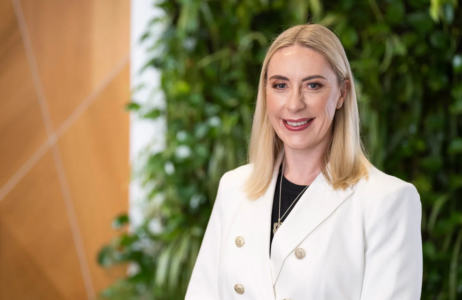 Carole in a white double breasted jacket in front of a living wall