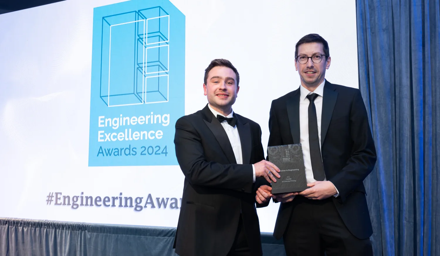 Ger being presented with the award trophy in front of a presentation screen