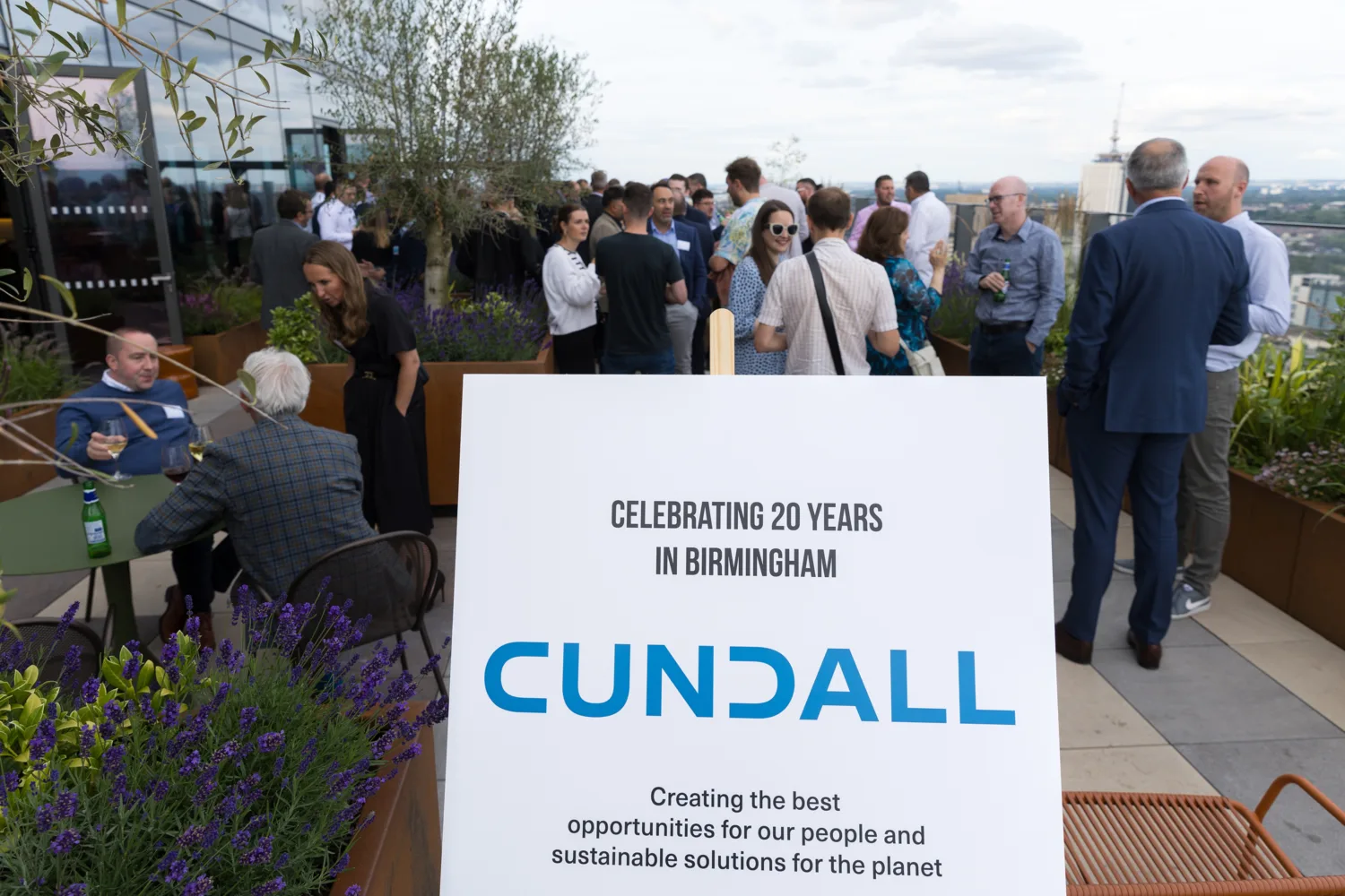 People socialising on an outdoor terrace with greenery and a board with Cundalls logo in the foreground