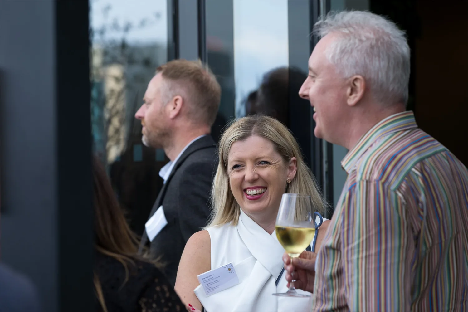 People smiling and holding a full wine glass in front of a glazed wall