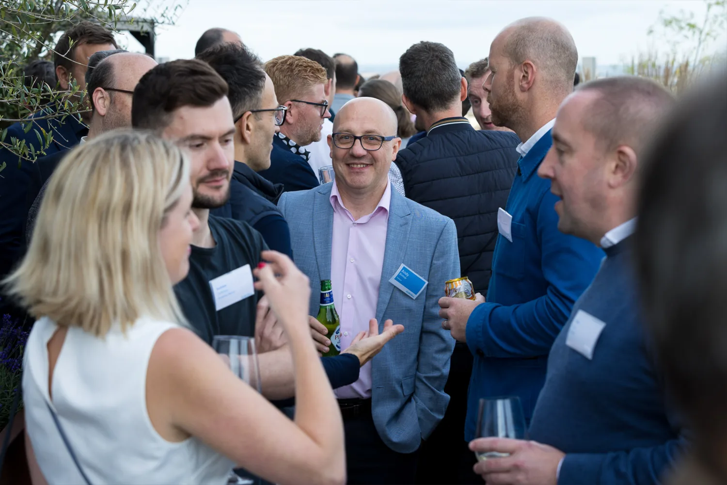 Central figure smiling to camera surrounded by people engaged in conversation outdoors