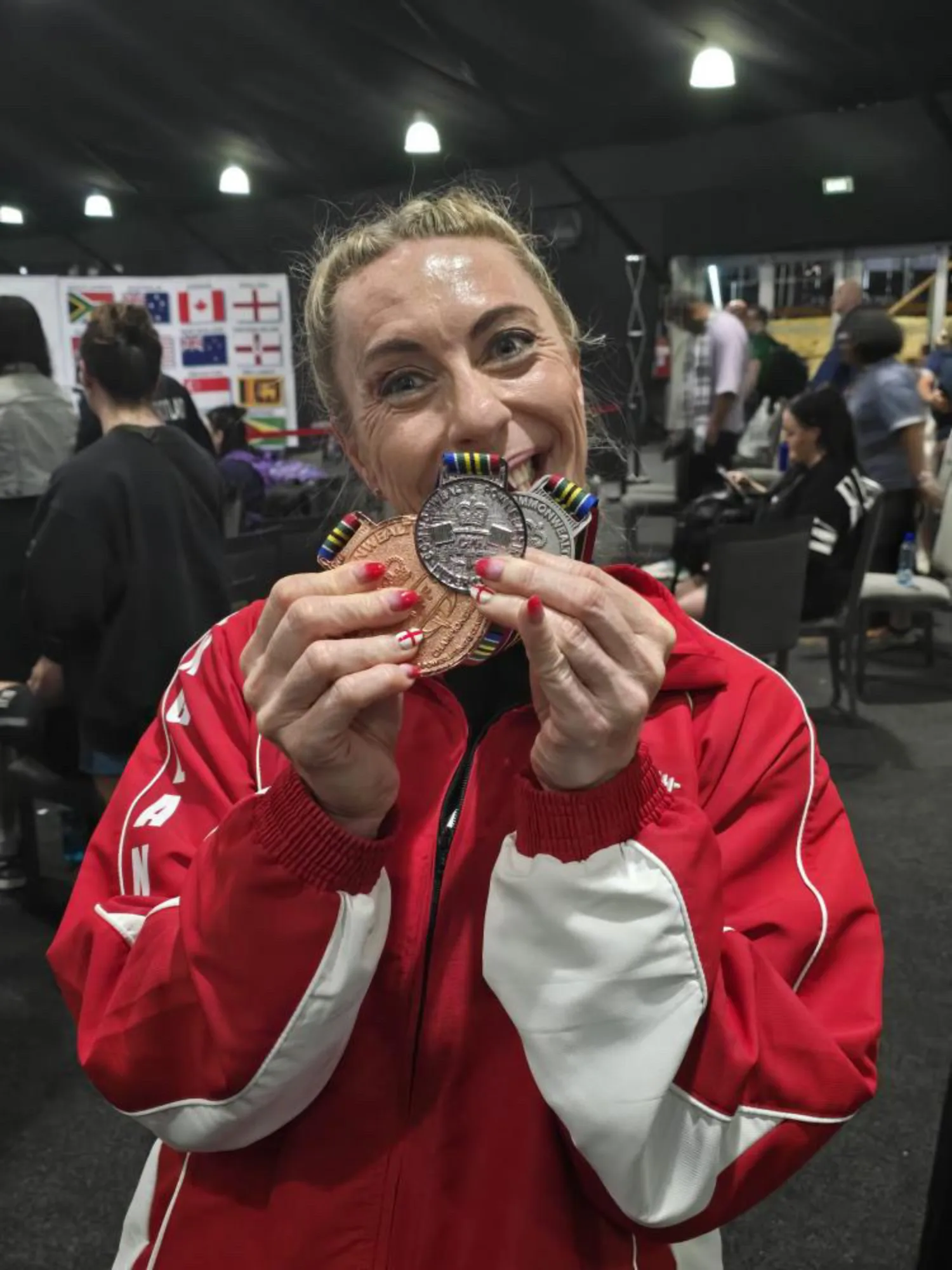 Carole O Neil at the Commonwealth Powerlifting Federation Championships in a red tracksuit holding medals