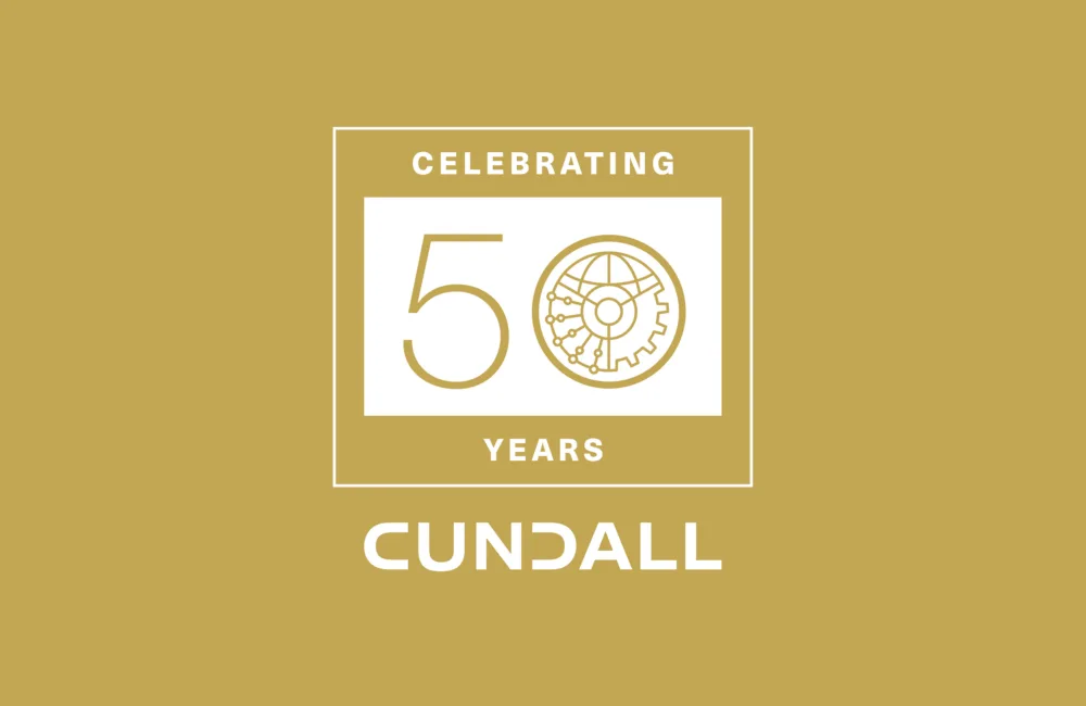 Gold background with a white rectangular frame containing the text “CELEBRATING 50 YEARS” and a circular graphic of a globe with connected lines and gear shapes. Below the frame, the word “CUNDALL” appears in bold white letters.