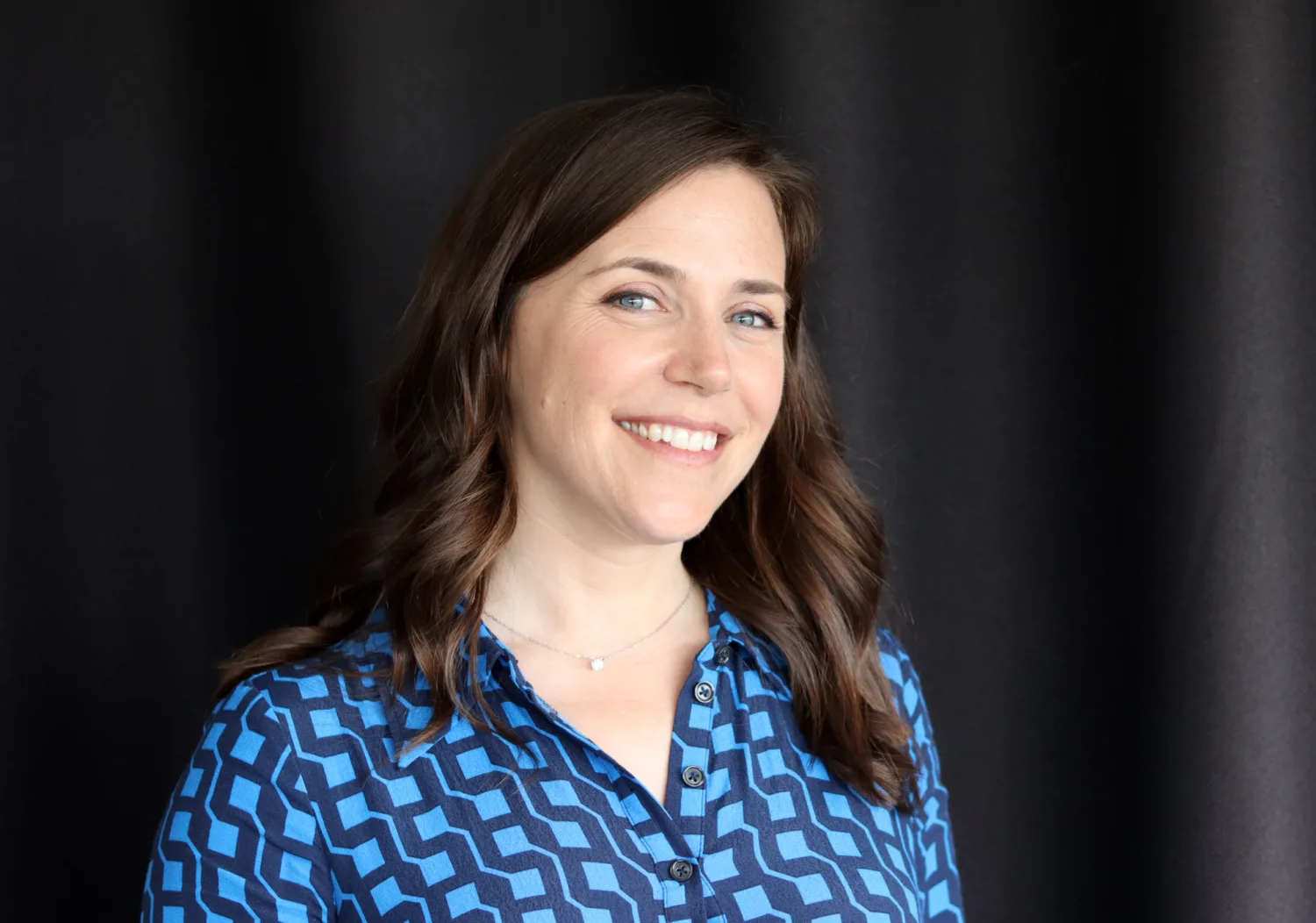Frances in a light and navy blue top against a dark background smiling to camera