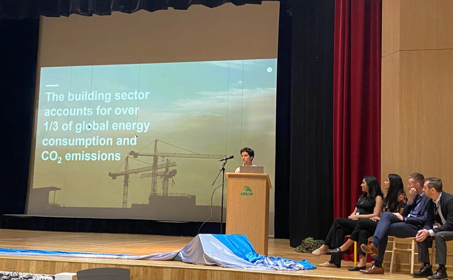 Sustainability engineer on stage behind a podium in front of a projected presentation