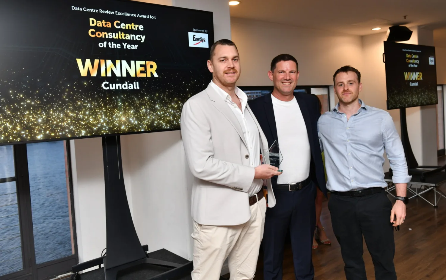 Team stood holding the glass award in front of a TV screen saying Data Centre Consultancy of the year WINNER Cundall.