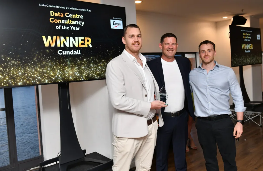 Team stood holding the glass award in front of a TV screen saying Data Centre Consultancy of the year WINNER Cundall.