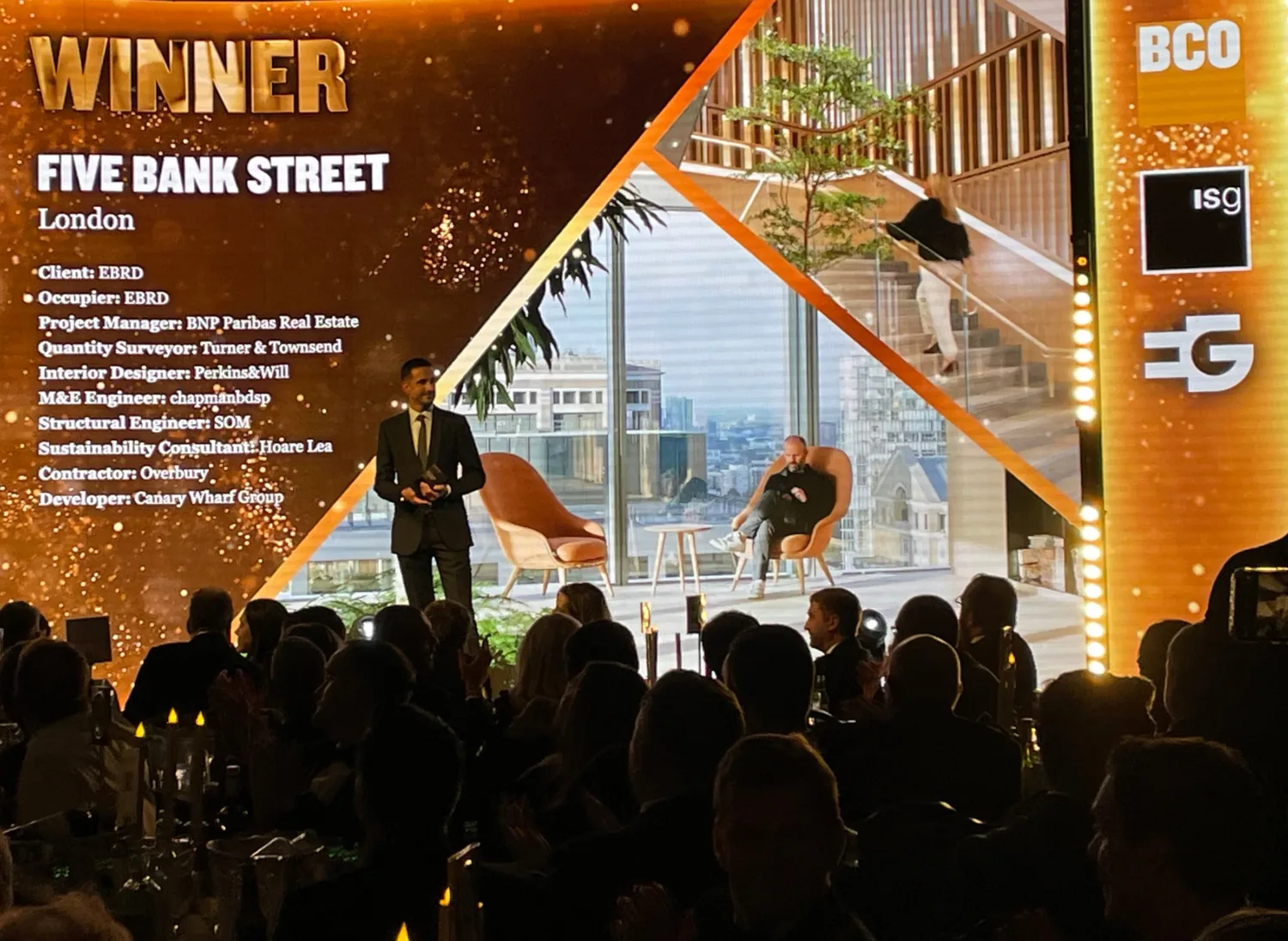 Awards presenter on stage in front of the WINNER Five Bank Street screen