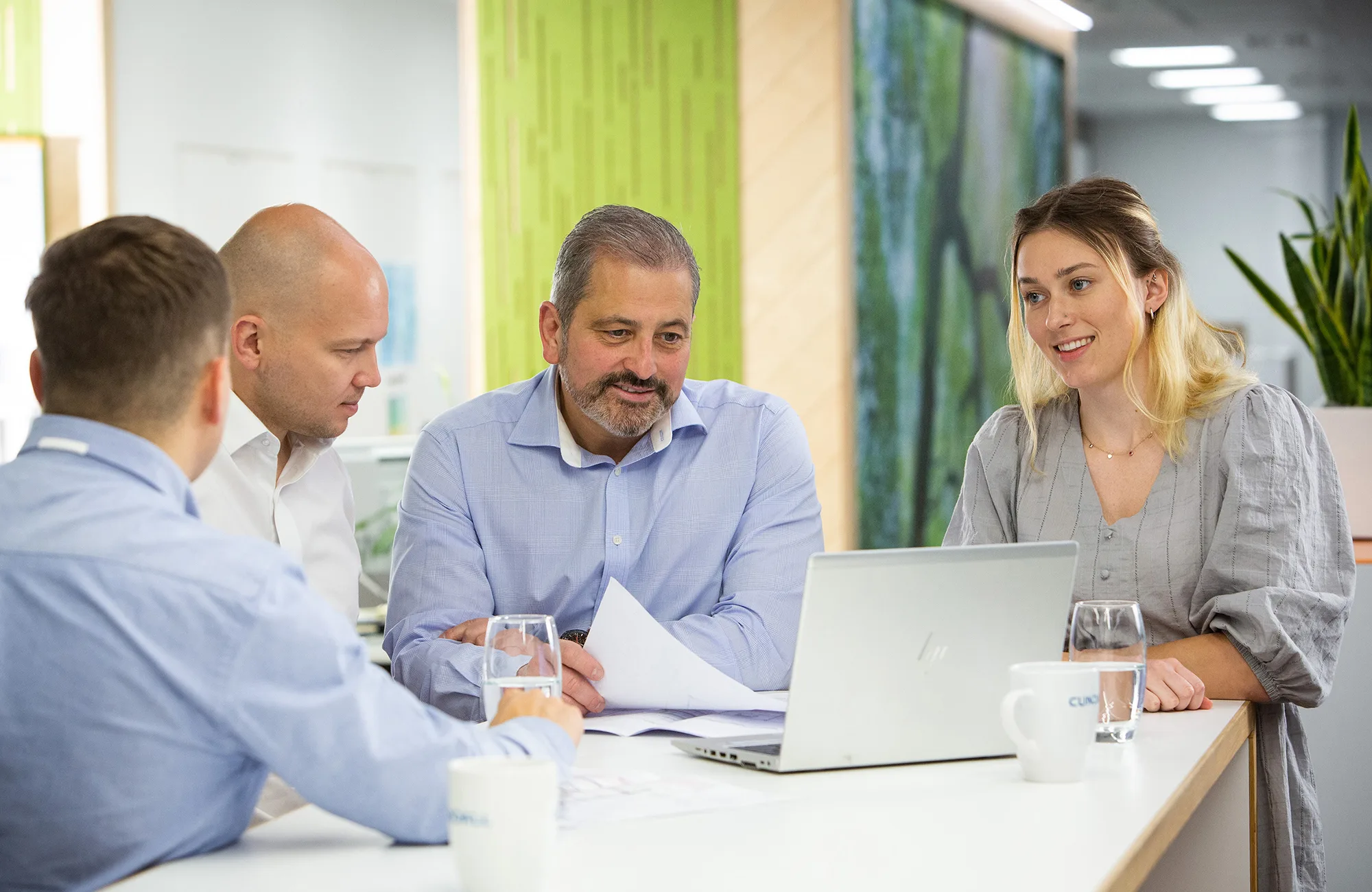 4 colleagues talking around a standing table with a laptop and papers