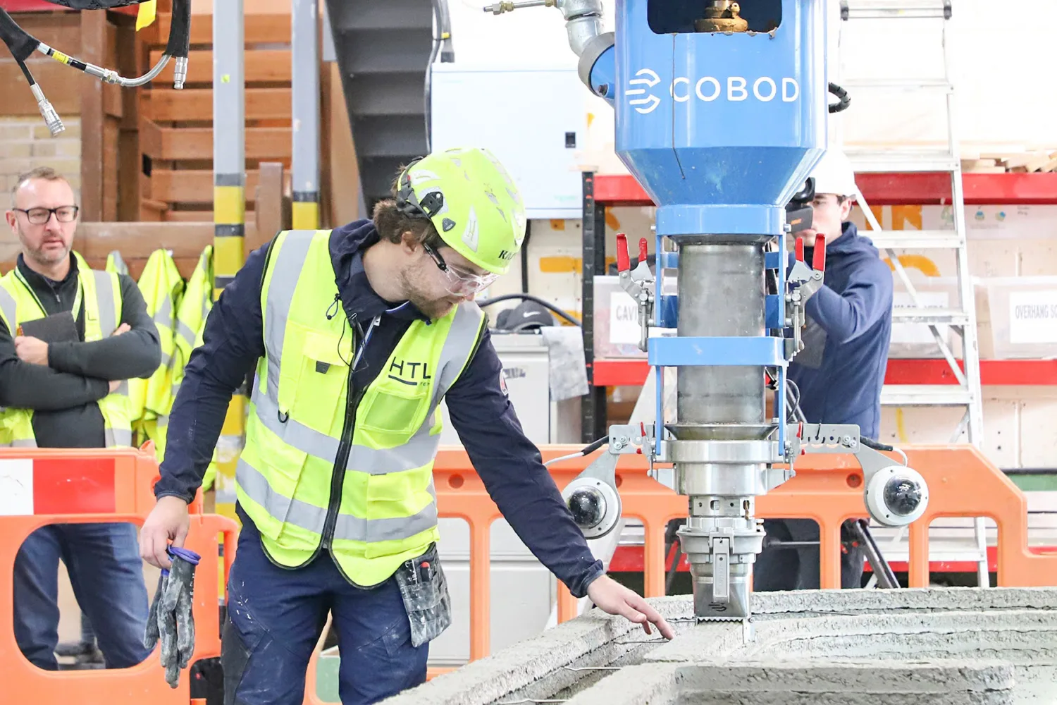 Workers in high vis jackets and hard hats overlooking a concrete printer on site