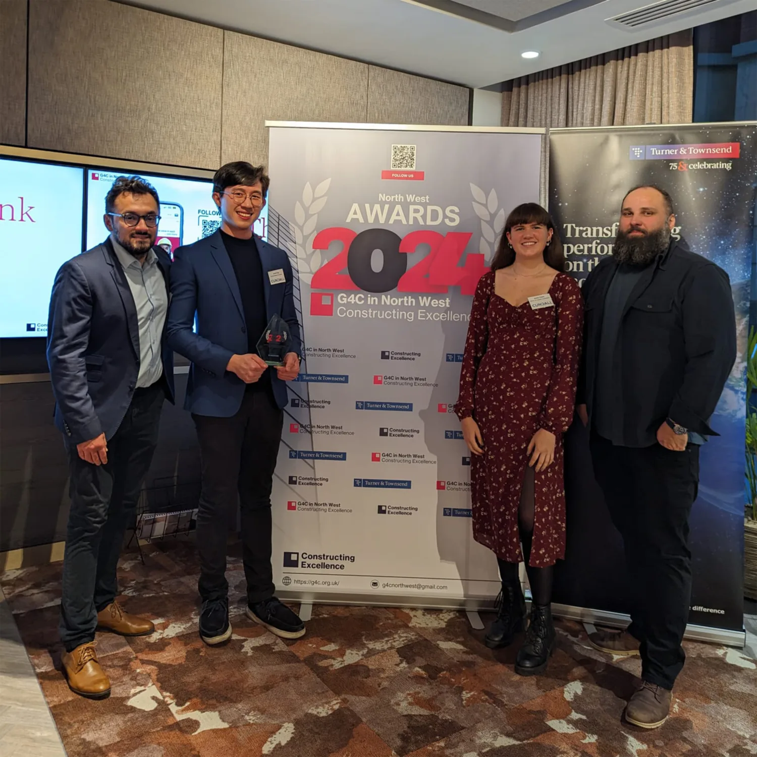 Jerryl holding the award standing with three other people in front of a North West Awards 2024 banner
