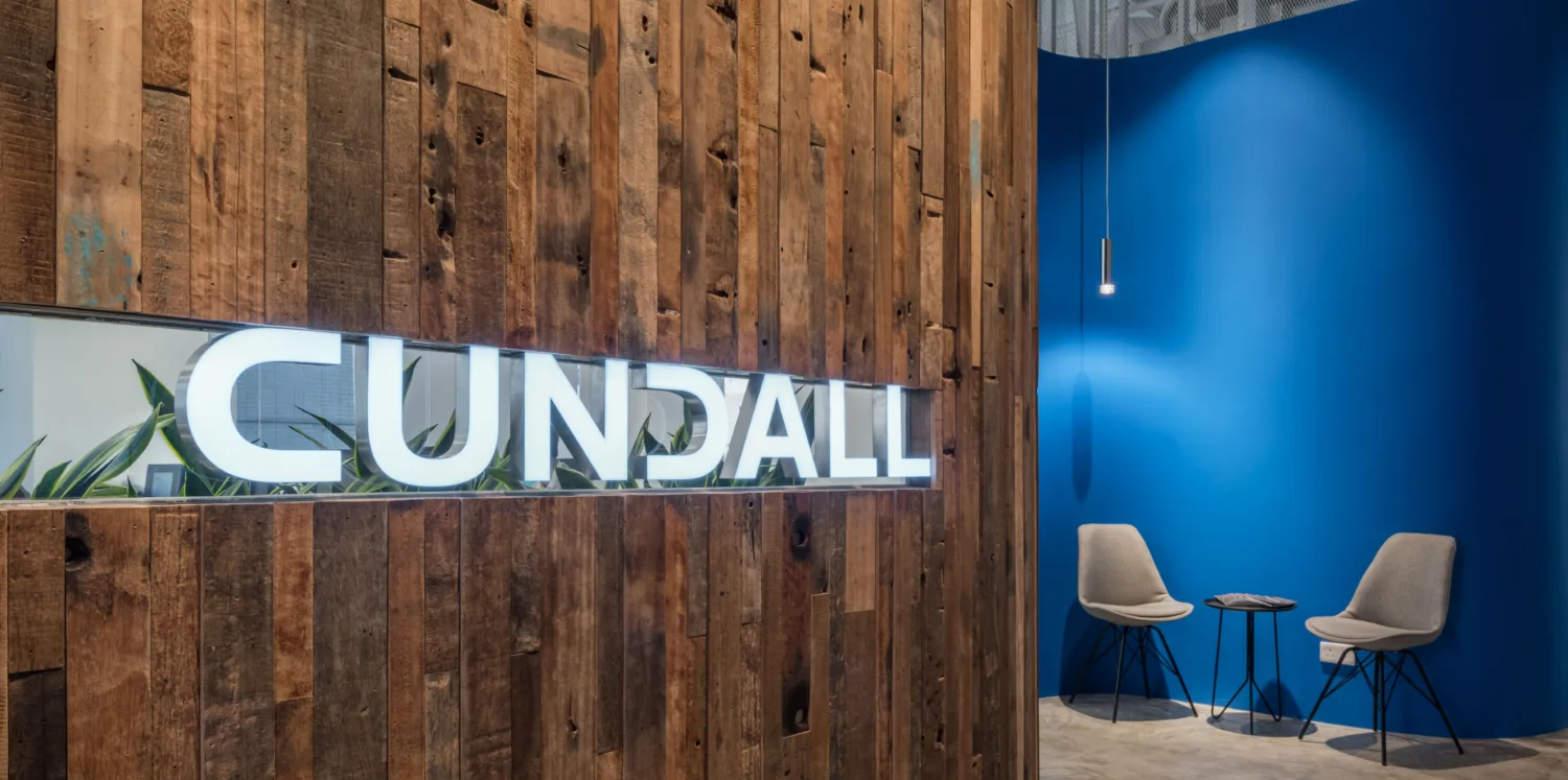 Wooden slat wall with lit Cundall logo with 2 chairs and small table against a blue wall