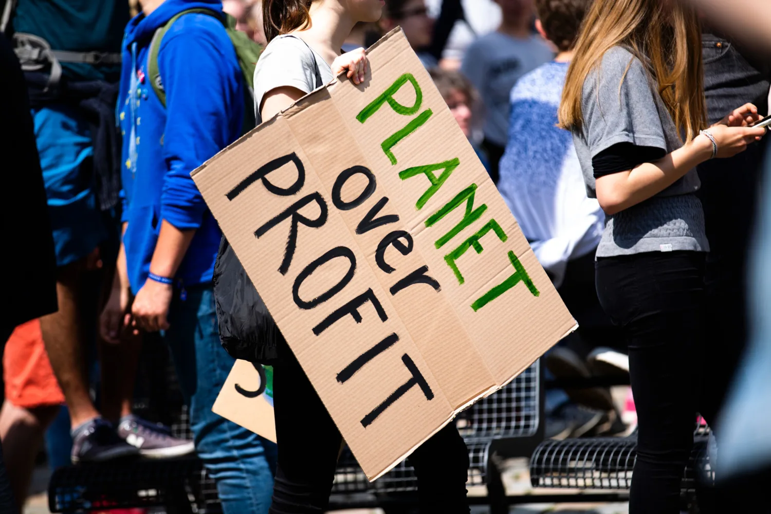 People at a protest carrying a carboard hand made sign that says 'Planet over profit'
