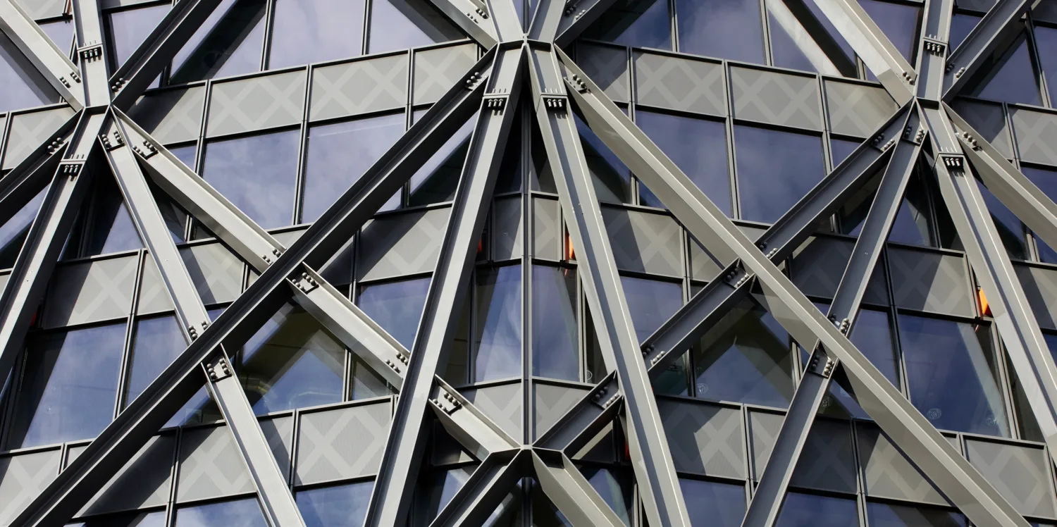 Close-up exterior of a windowed office building, with metallic beams arranged across the outside in a geometric pattern