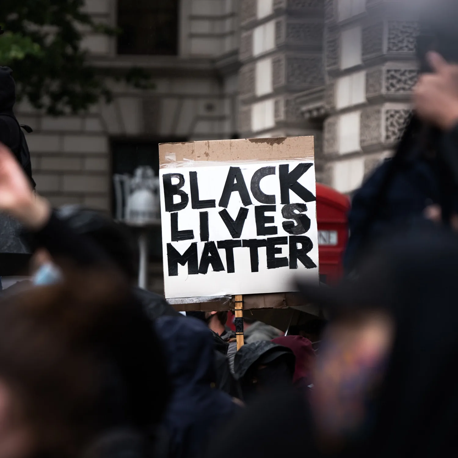 A group of unidentifiable people at a protest, one is holding a sign that reads in all capital letters 'Black Lives Matter'