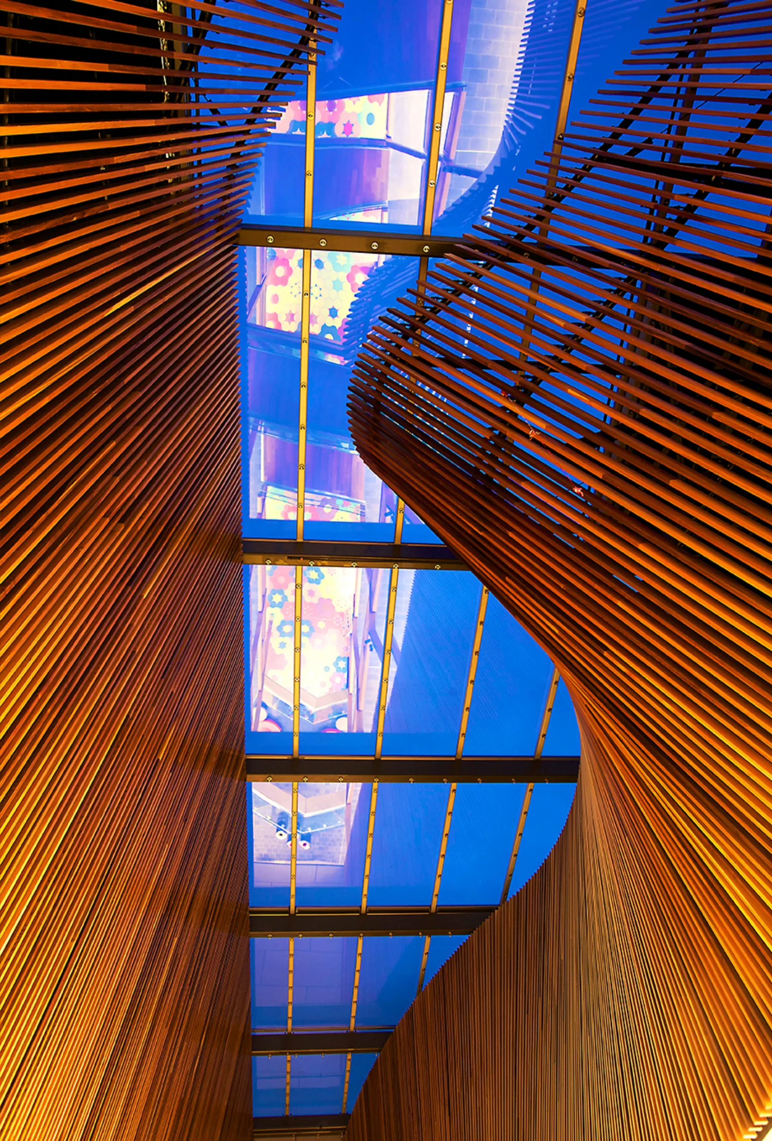 Interior of a modern building, strips of wood arranged in a curving pattern, all pointing towards a clear glass ceiling
