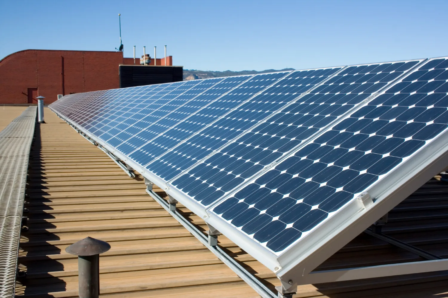 Row of angled solar panels on a wood-panelled roof, in the background a red bricked structure is visible