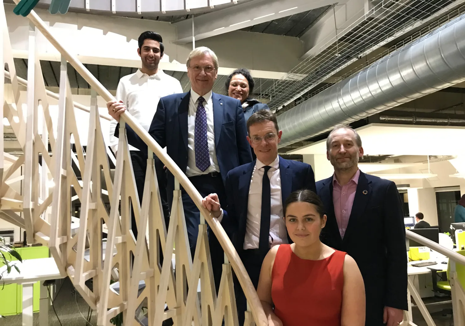Six smiling people standing on the wooden spiral stairs on the Cundall Birmingham office