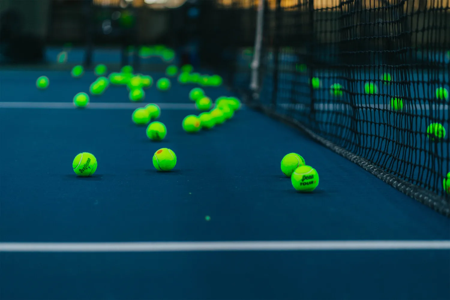 Fluorescent green tennis balls sitting on a dark blue tennis court