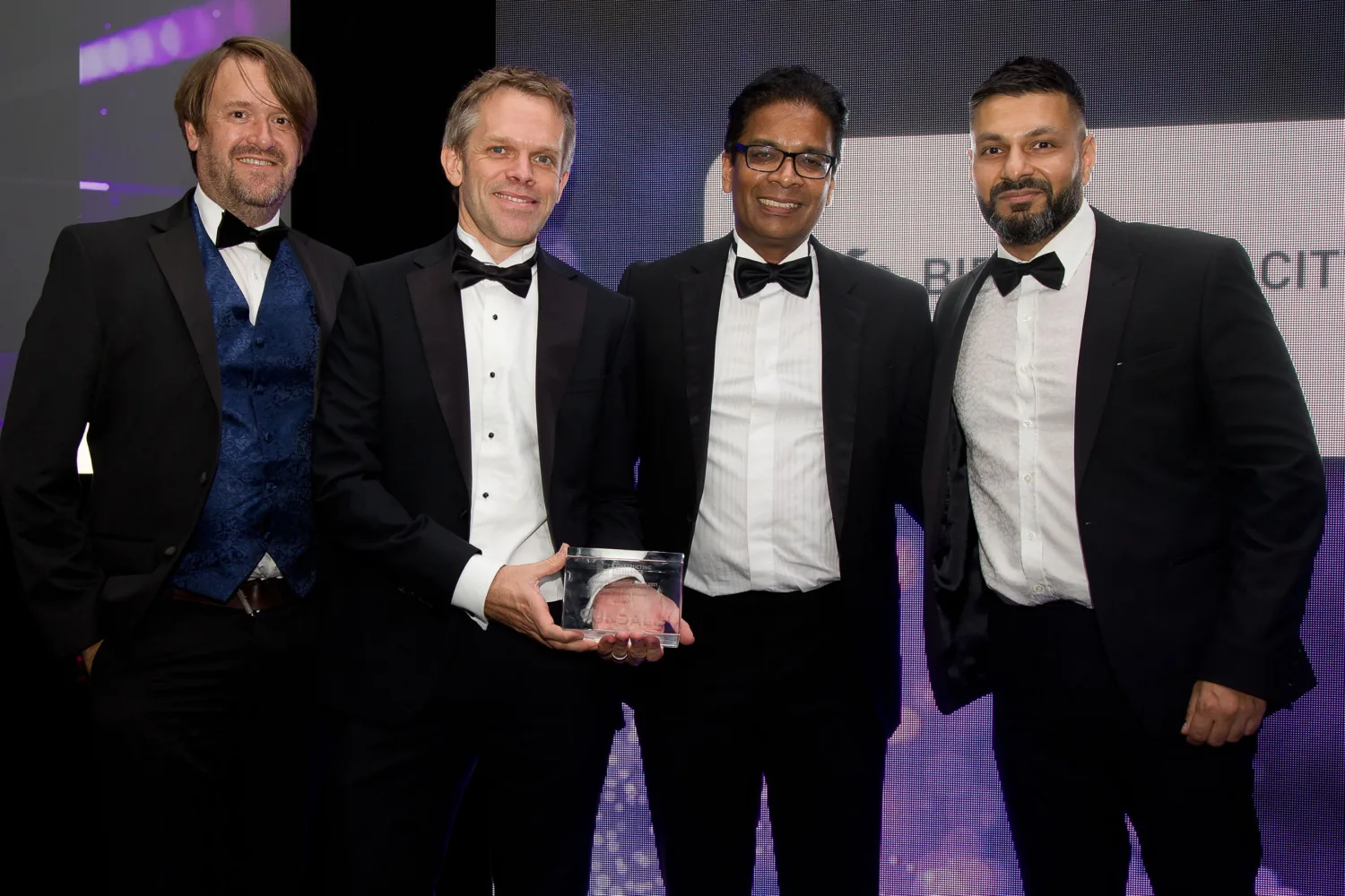 The team in suits and bow ties holding the award on stage