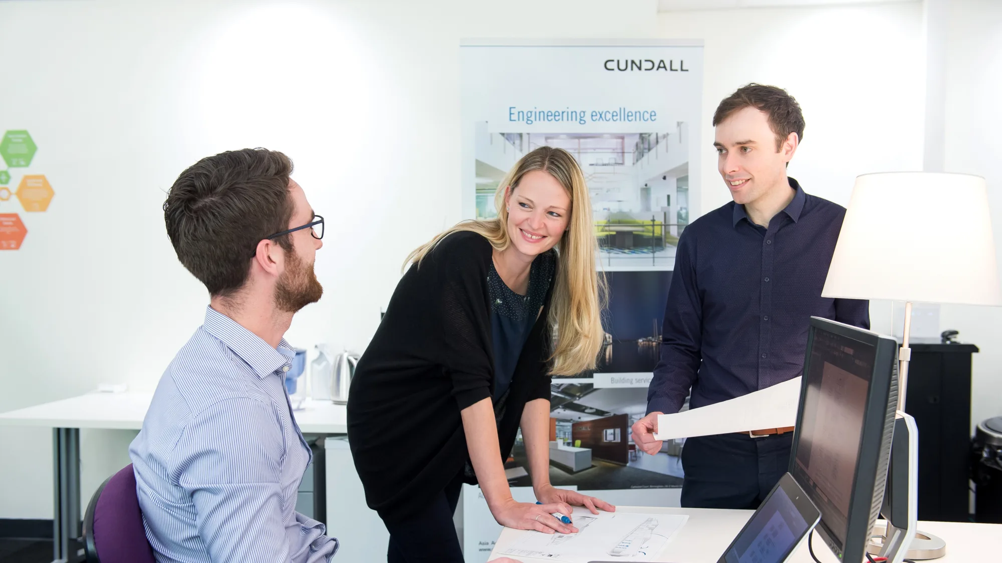 Lewis Hewton with colleagues discussing project at desk with computer