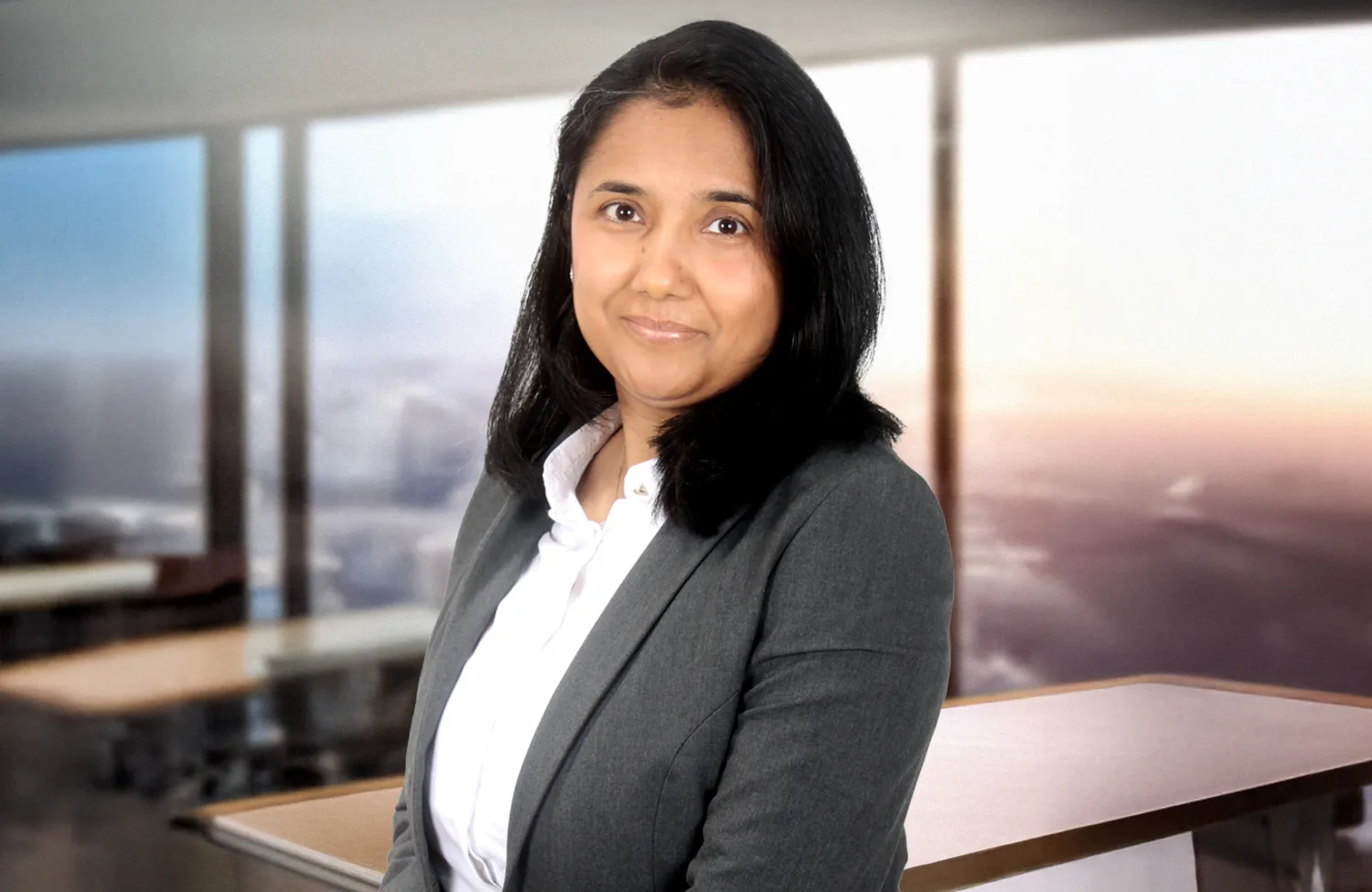 A cut out of Priya in a white shirt and grey suit jacket superimposed on an AI office background