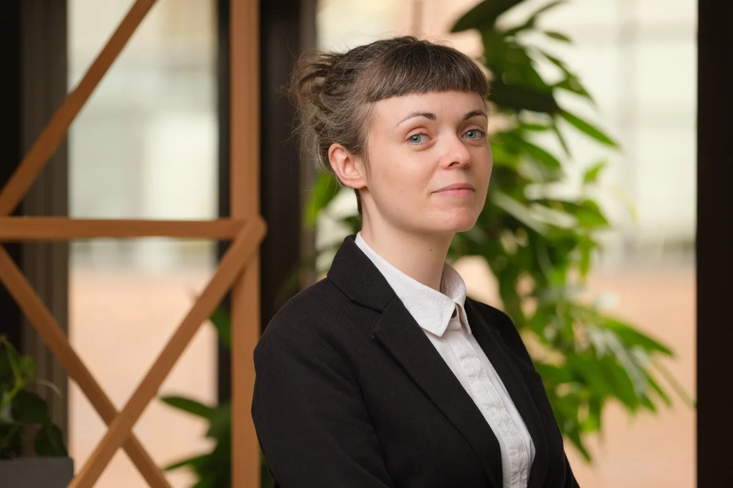 Kim standing in front of wooden trellis wearing a black blazer and a white shirt.