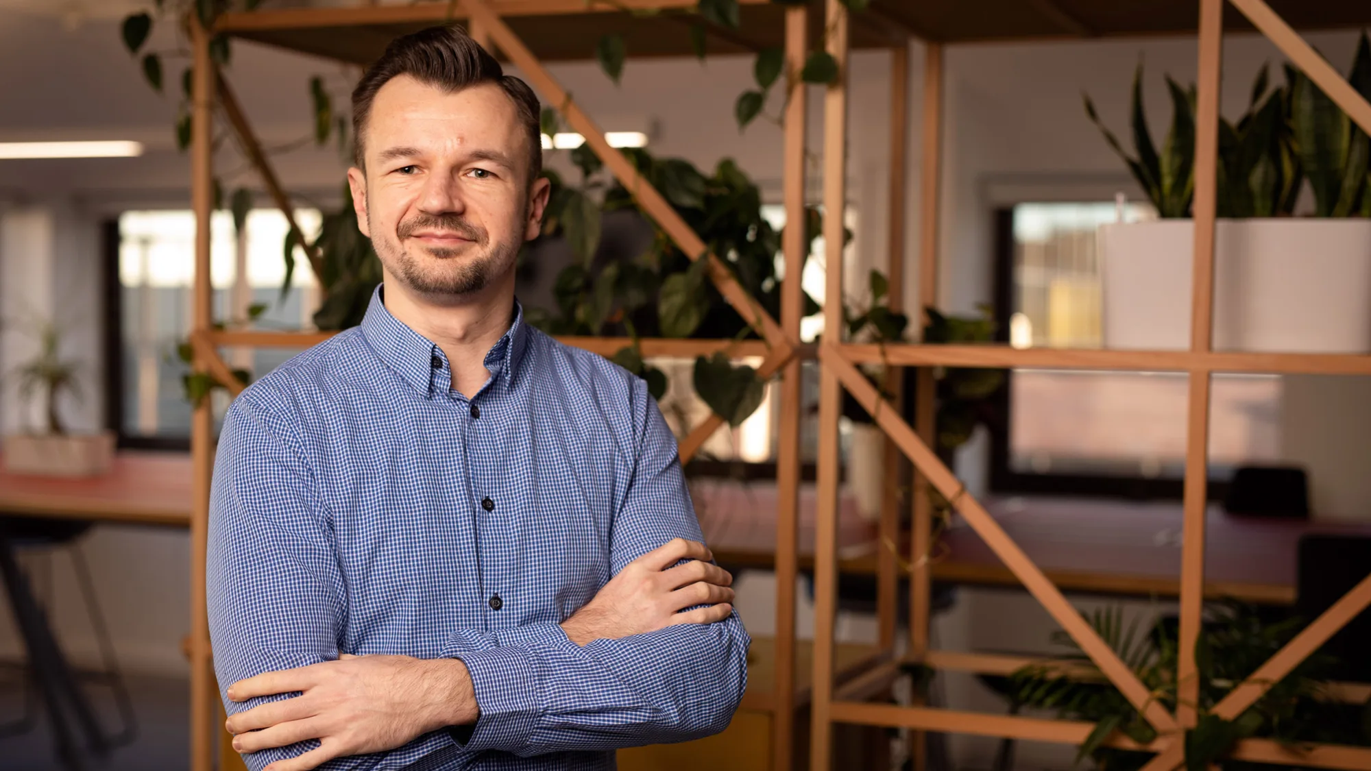 Maciej stood in a blue shirt with arms folded in front of a wooden shelving structure