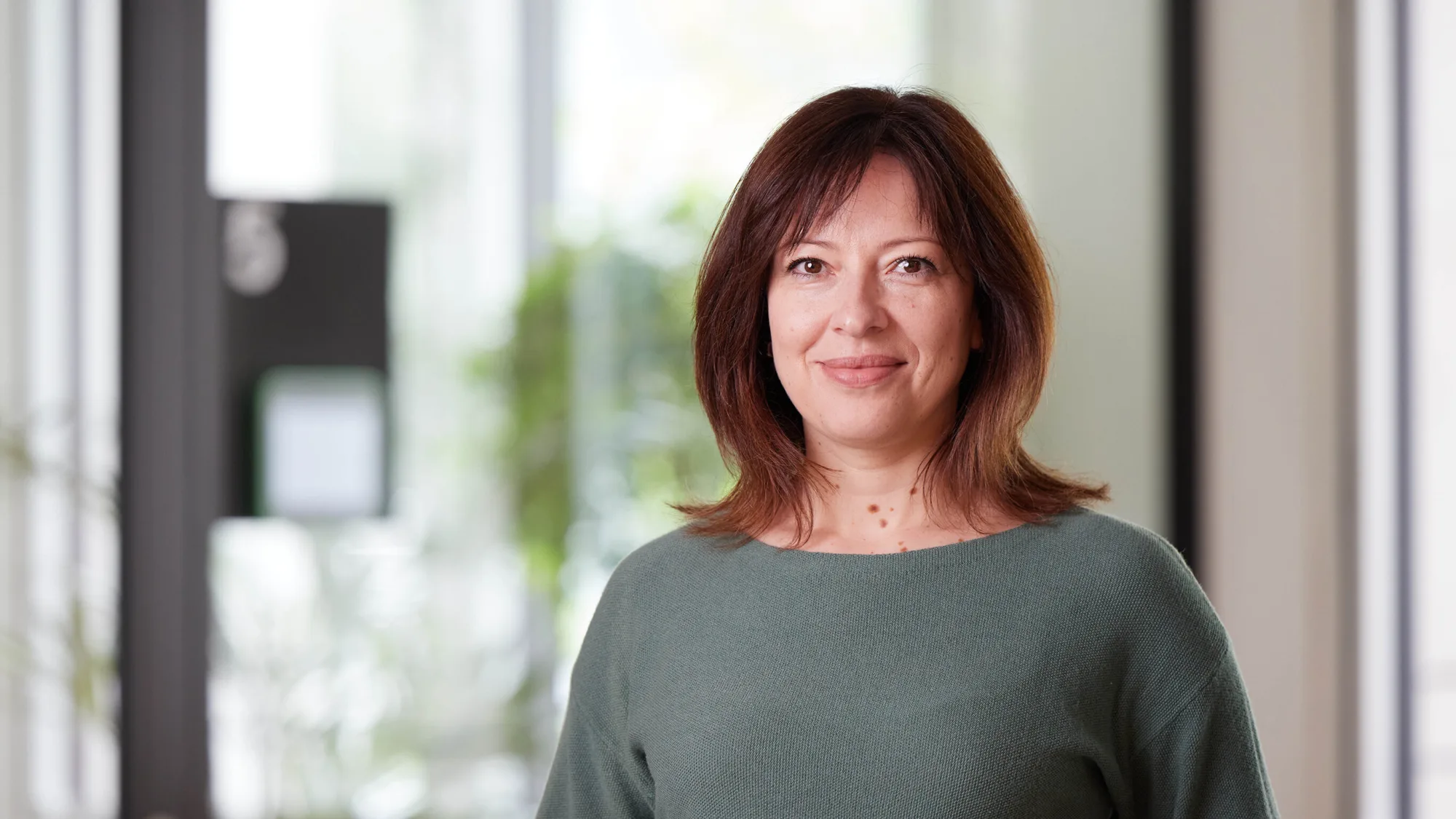 Natalia in a green top stood smiling to camera with a blurred office background