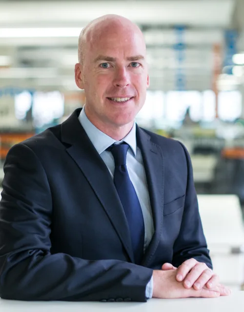 Paul Chatwin in a navy suit with sat at a high table with the office behind