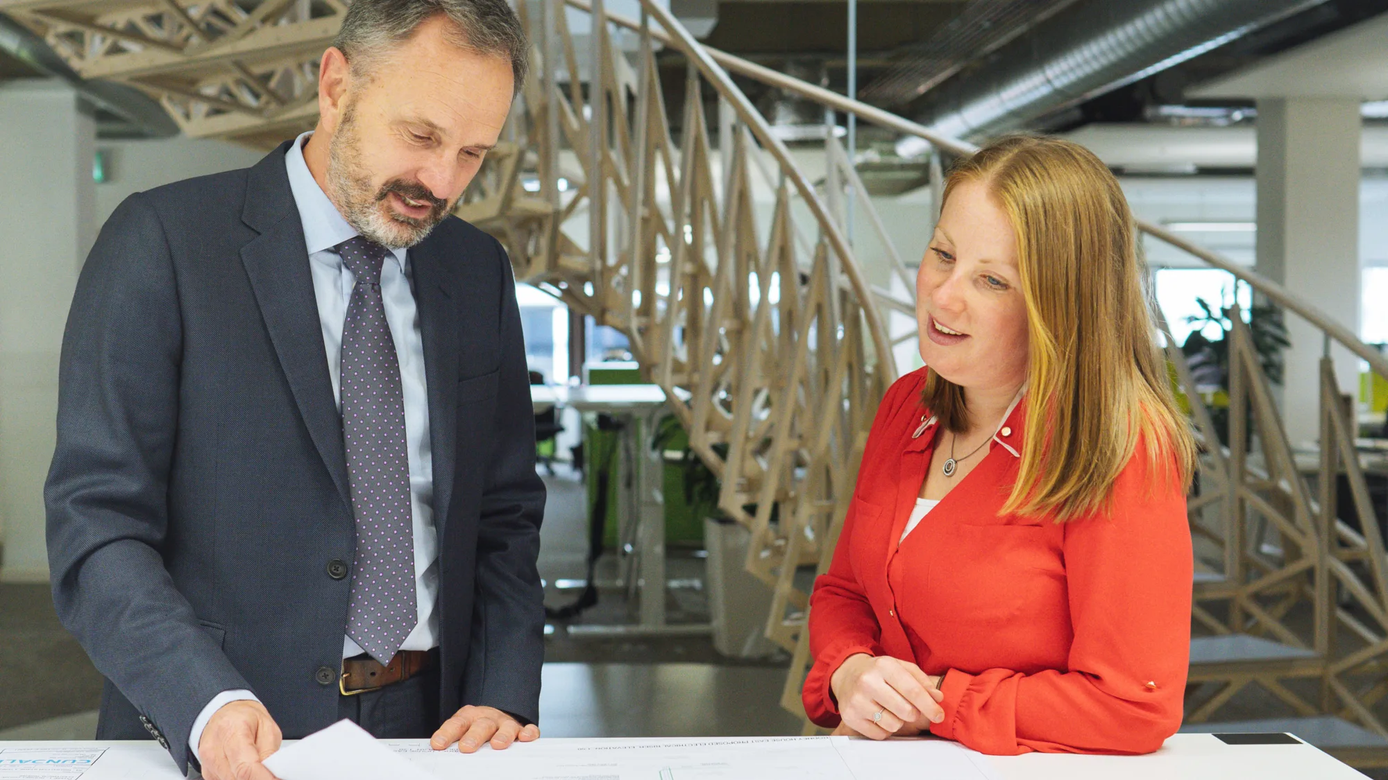 Rob van Zyl in meeting with colleague at a hot desk with drawings and a staircase feature behind