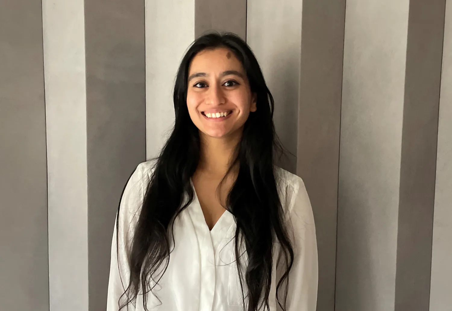 Rowshi Hussain in a white shirt in front of a panelled wall