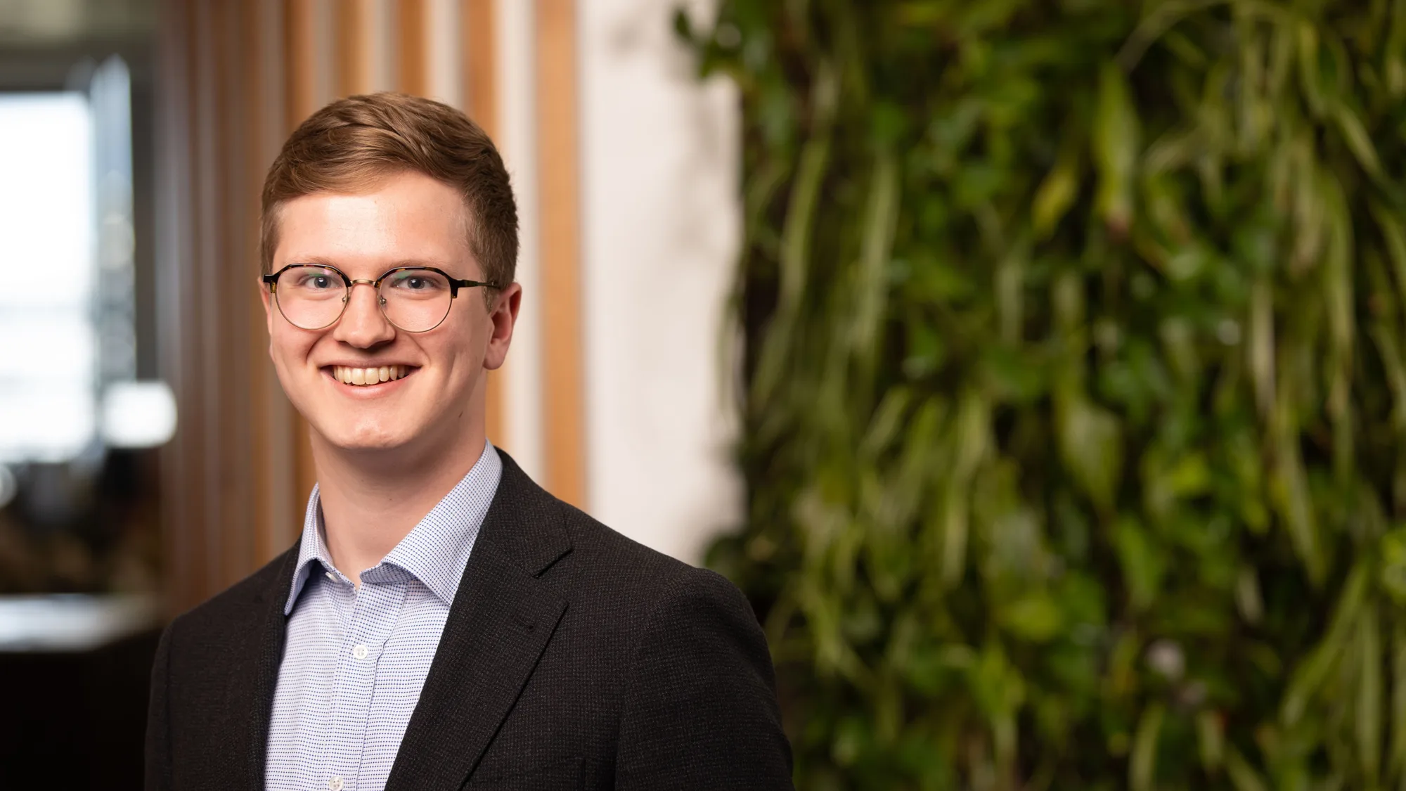 Tim in a blue shirt and suit jacket in front of a living wall