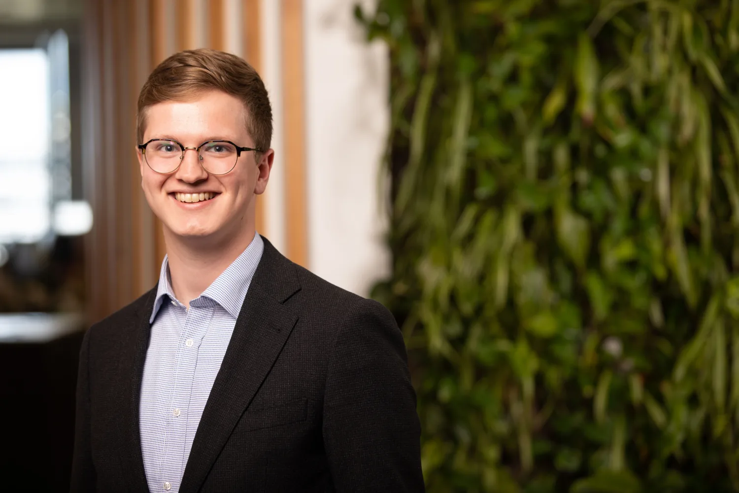Tim in a blue shirt and suit jacket in front of a living wall