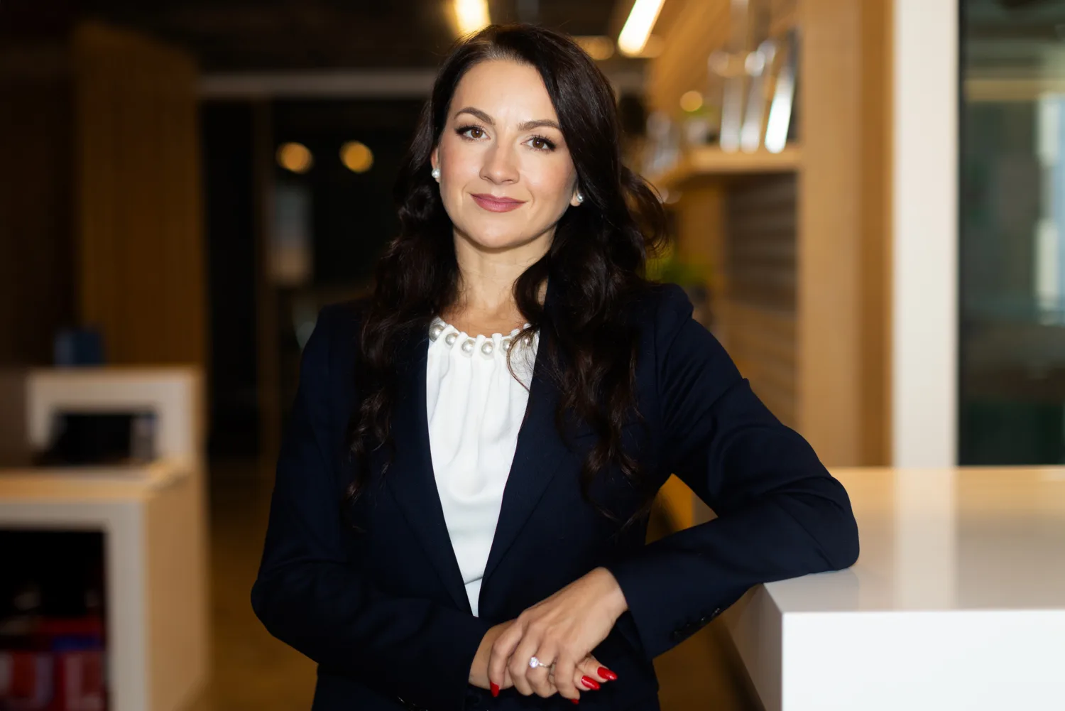Olga in a white top and dark jacket looking to camera in the office